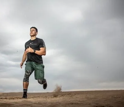 pexels-photo-2827392-2827392 A muscular man running on sandy terrain under cloudy skies, promoting fitness and adventure.