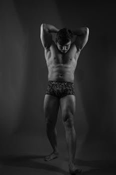 A studio shot of a muscular man flexing his muscles in a black and white style.