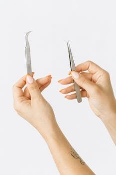 A pair of hands holding metal tweezers against a white background, showcasing manicure.